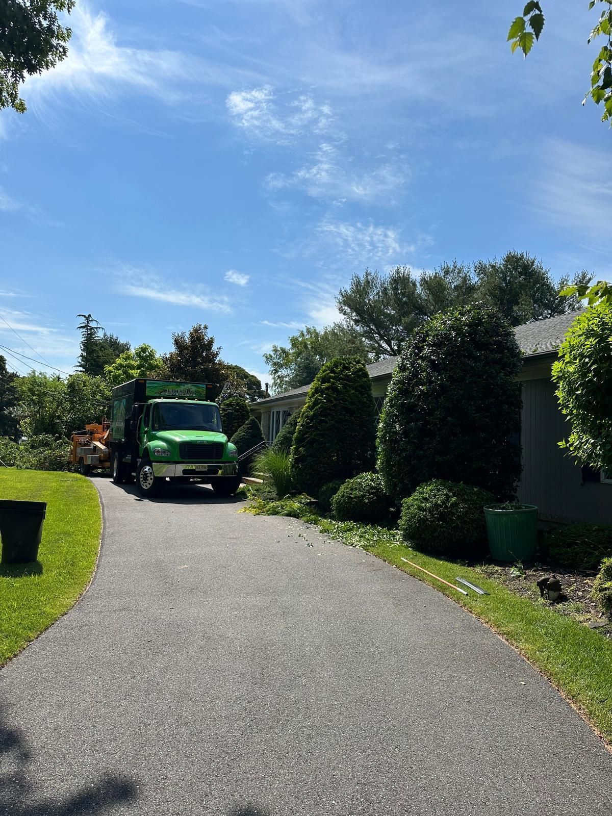 Green truck on a gravel driveway between trimmed hedges under a bright blue sky.