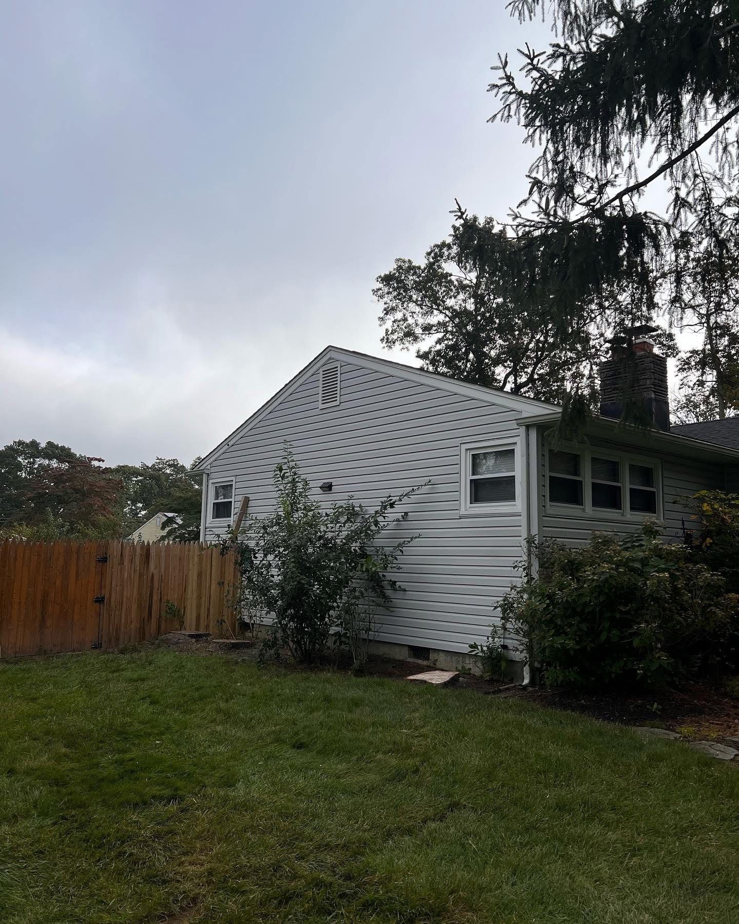 White house with gray roof beside a wooden fence and green lawn under a cloudy sky