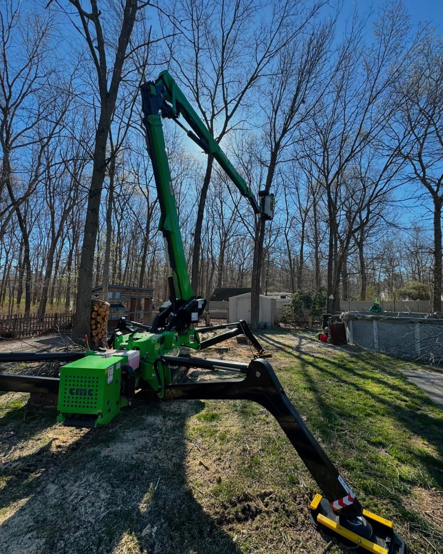 Green forestry machine with extended boom in a wooded yard under a blue sky