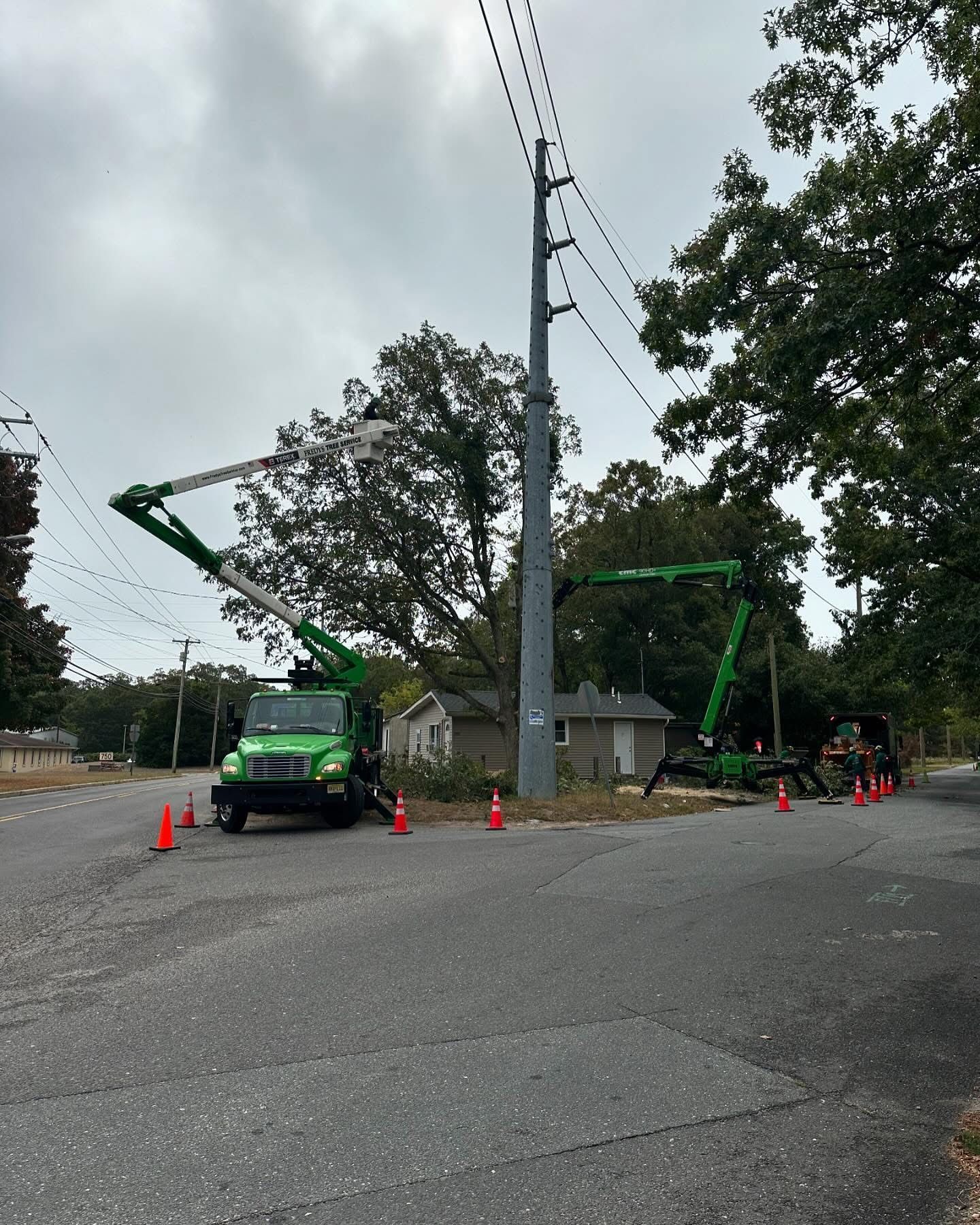 Utility trucks and bucket lifts working by a roadside beside a small building and utility pole.