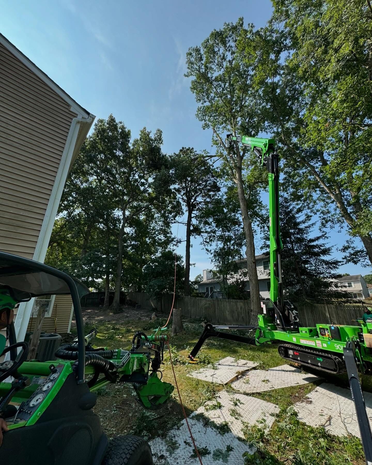Green construction equipment in a backyard beside a house, with trees and blue sky.