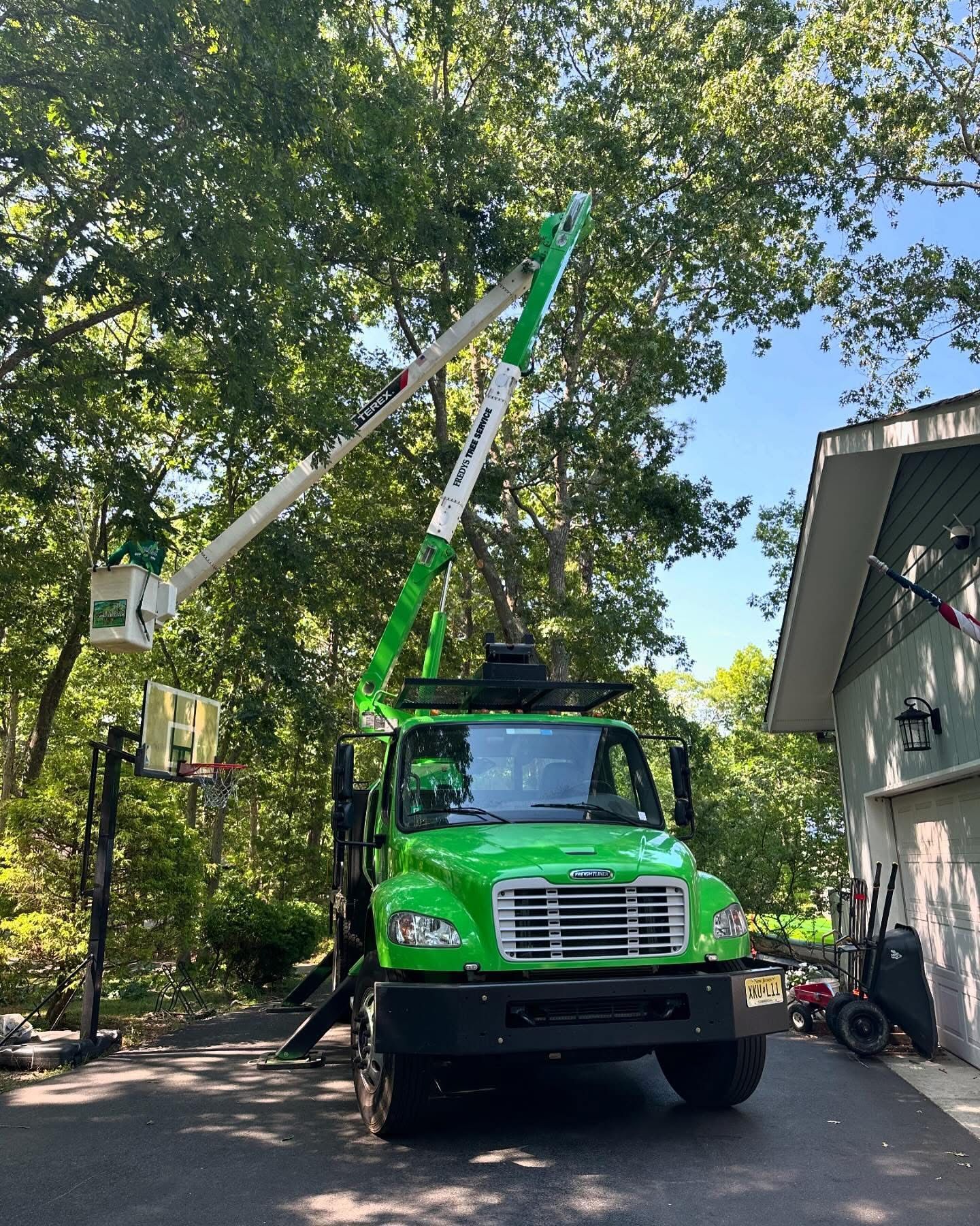 Green utility truck with raised boom arm parked beside a house in a wooded driveway
