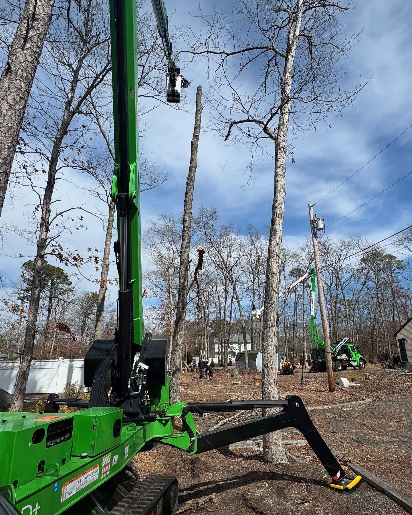 Green crane truck lifting a worker in a wooded area under a blue sky