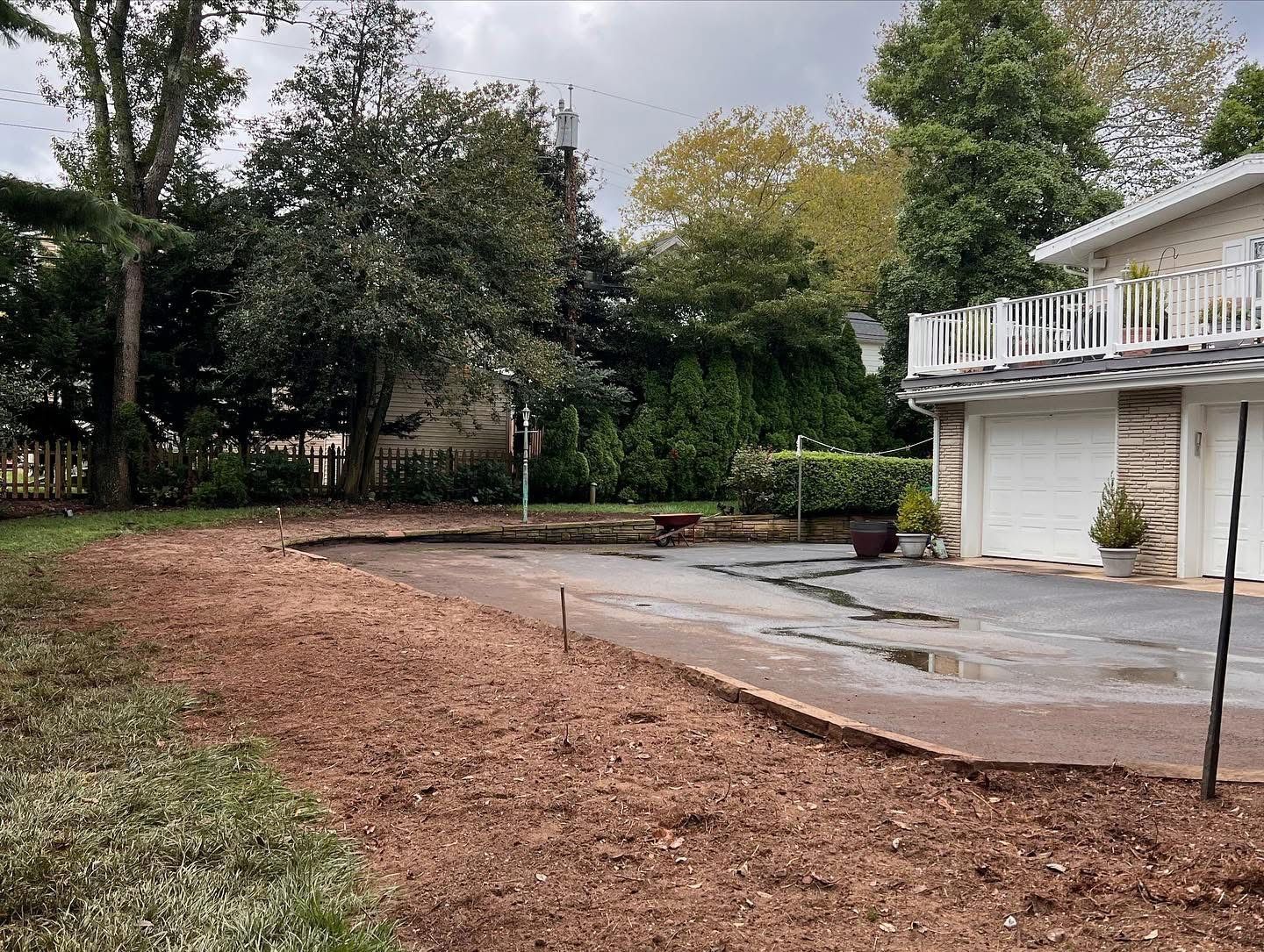 Empty driveway beside a white garage and house, with wet pavement and trees in the background.