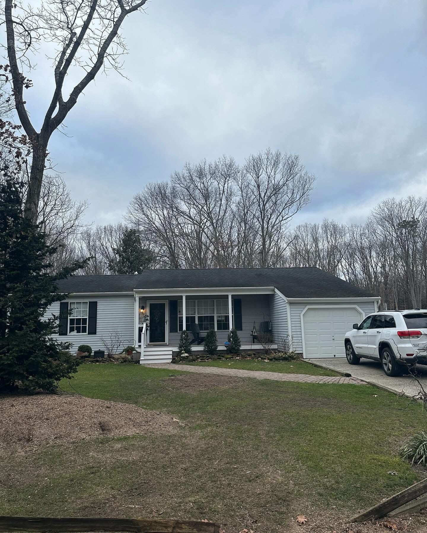 Single-story gray house with white porch and garage, driveway, and a white pickup in a wooded neighborhood.
