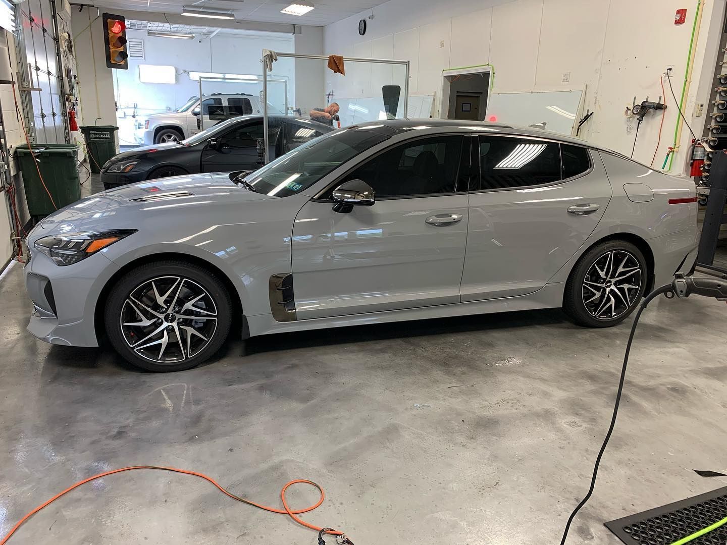 Gray Kia Stinger with tinted windows parked inside a car detailing shop, surrounded by equipment.
