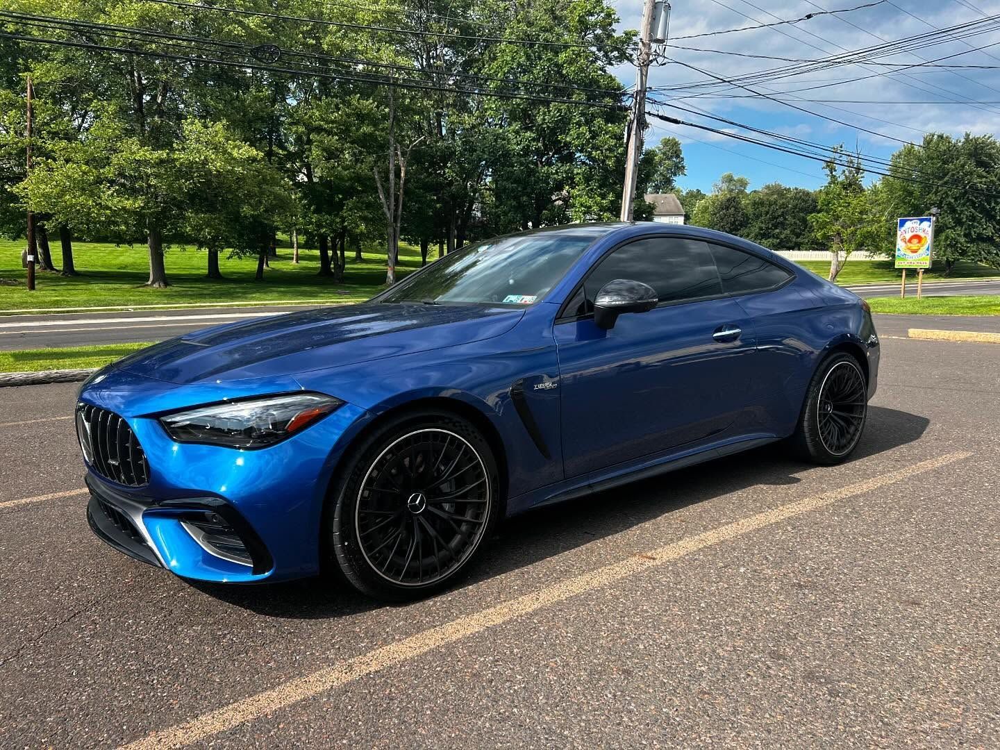 Blue Mercedes-AMG coupe parked on asphalt; trees and sky in the background.