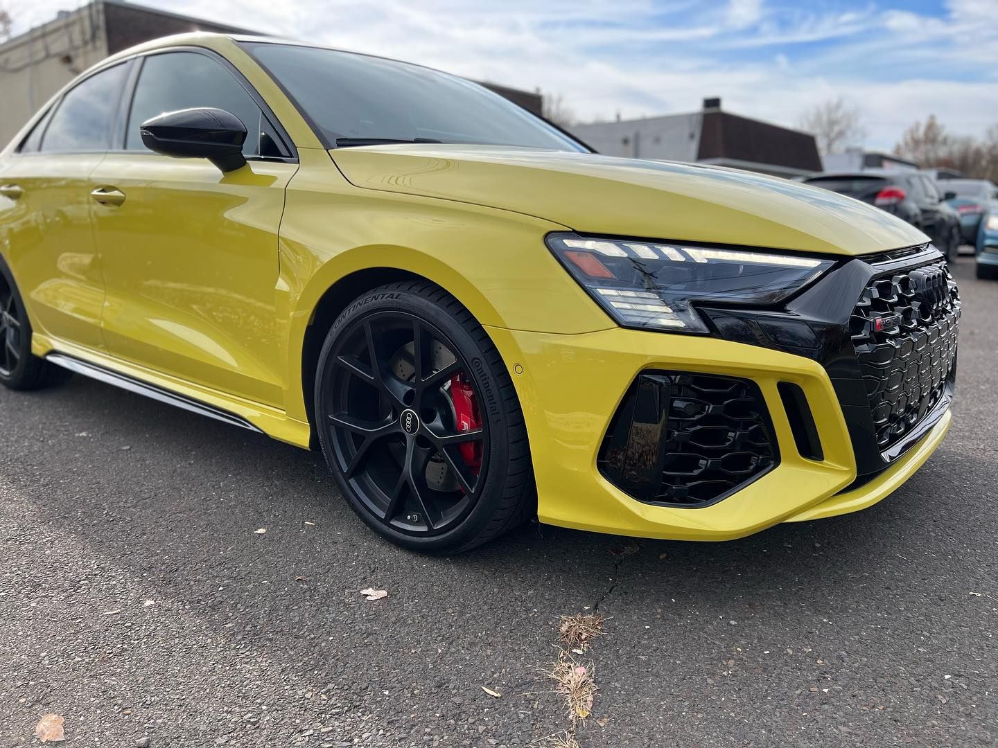 Yellow Audi RS3 sedan, black wheels, red brake calipers, parked outdoors.