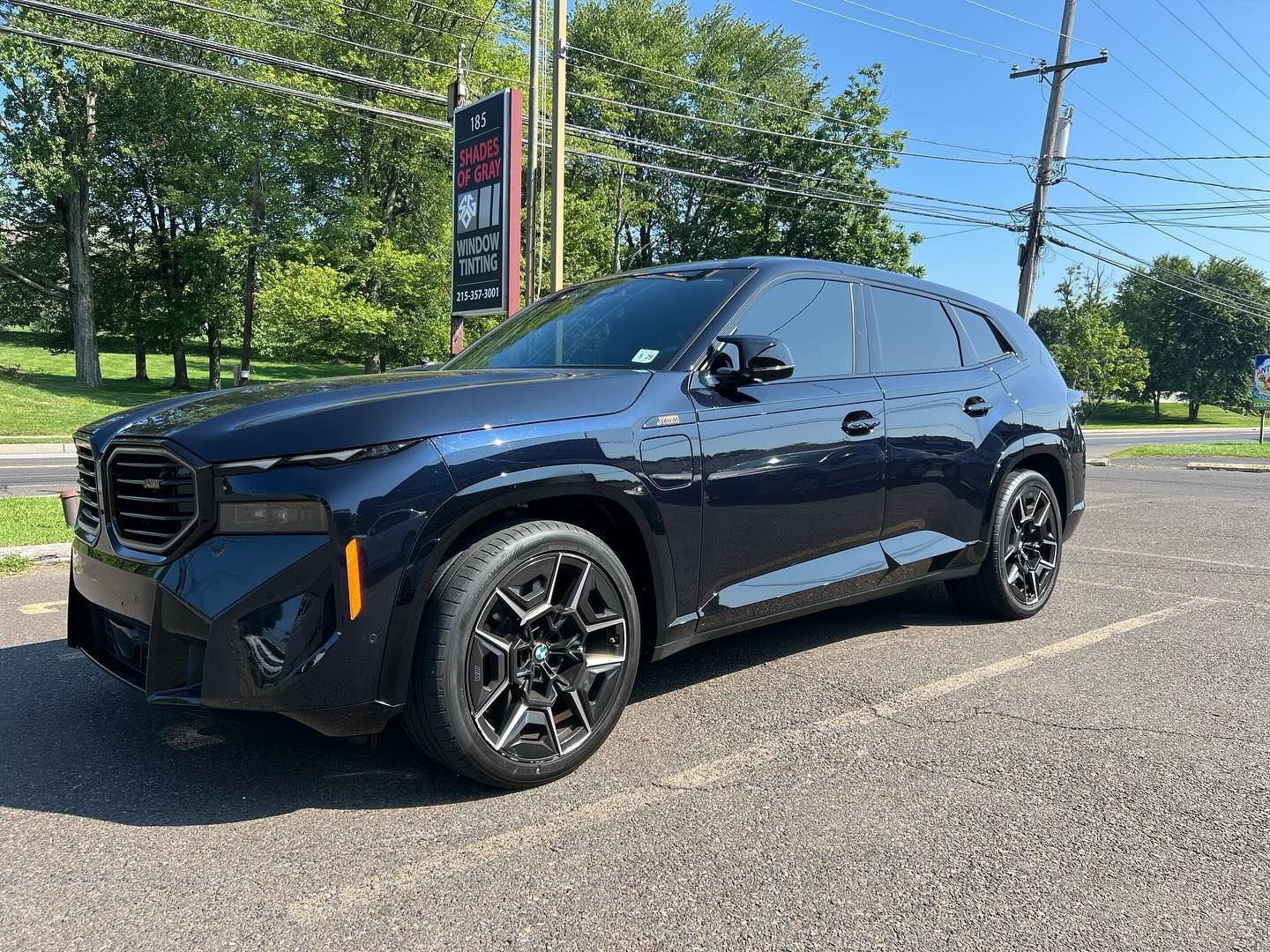 Dark blue BMW XM SUV parked on asphalt, sunny day.