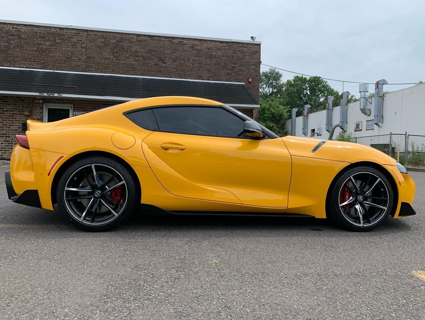 Yellow Toyota Supra sports car parked outside a brick building.