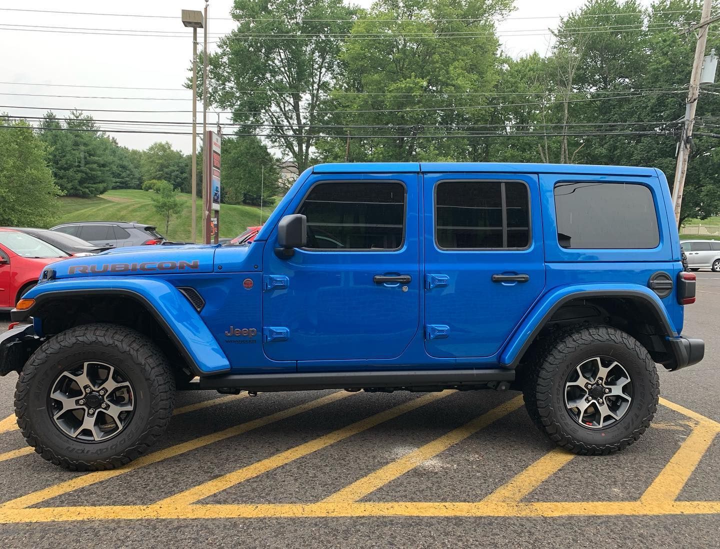 Blue Jeep Wrangler parked on asphalt, tinted windows, dark wheels, dealership setting.