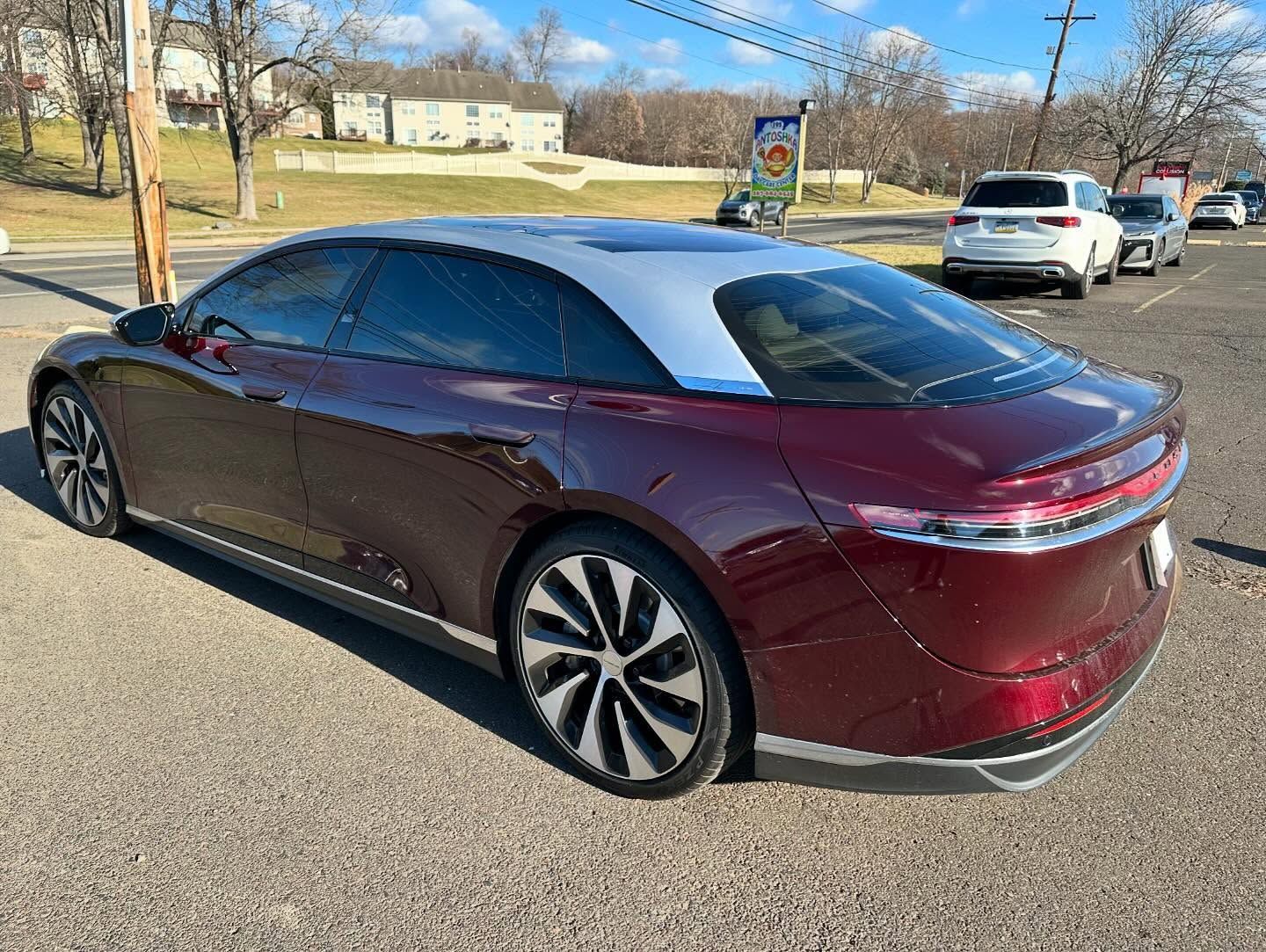 Maroon Lucid Air electric car parked on a paved road; blue sky in background.