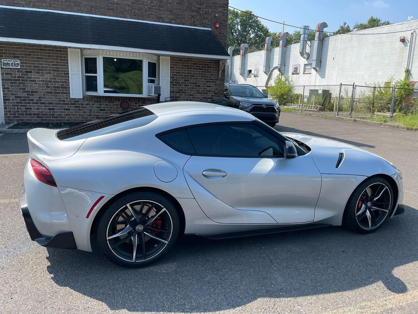 Silver Toyota Supra parked outside a brick building on a sunny day.