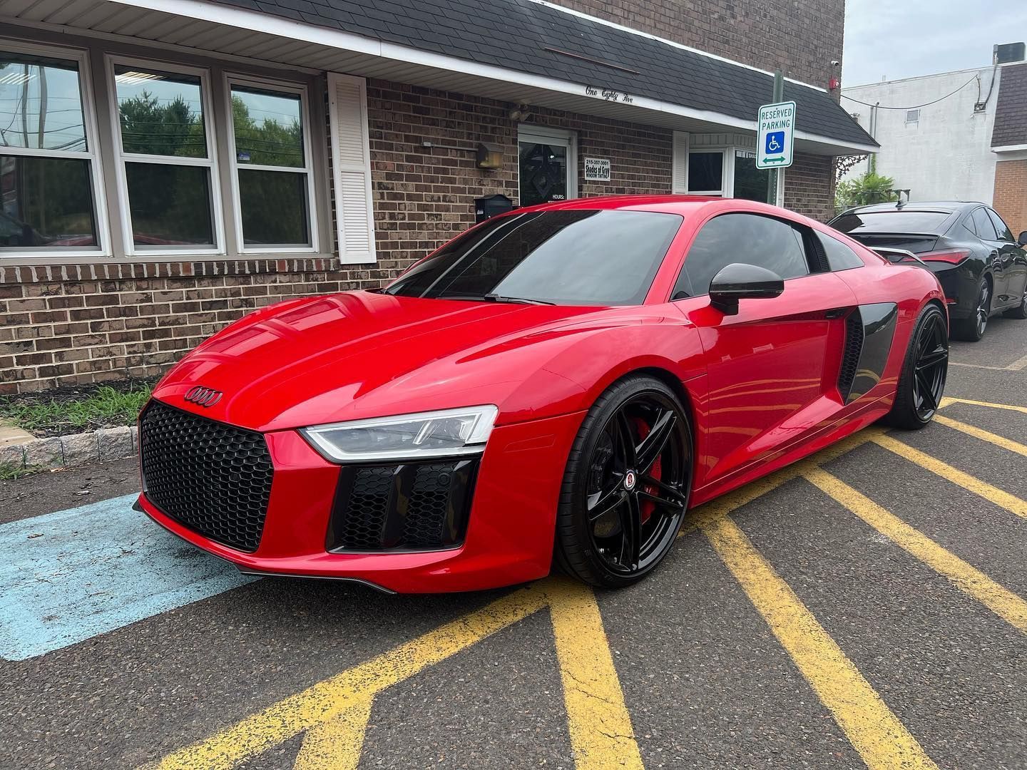 Red Audi R8 parked on a striped street in front of a brick building.