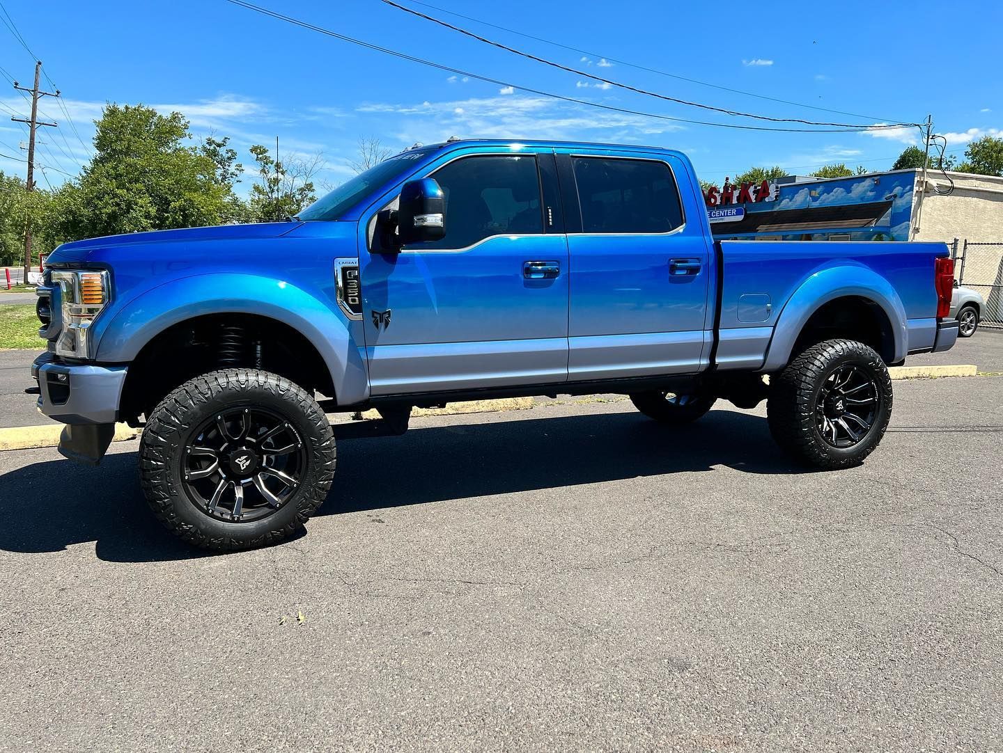 Blue pickup truck with black wheels, parked on asphalt, bright sunny day.