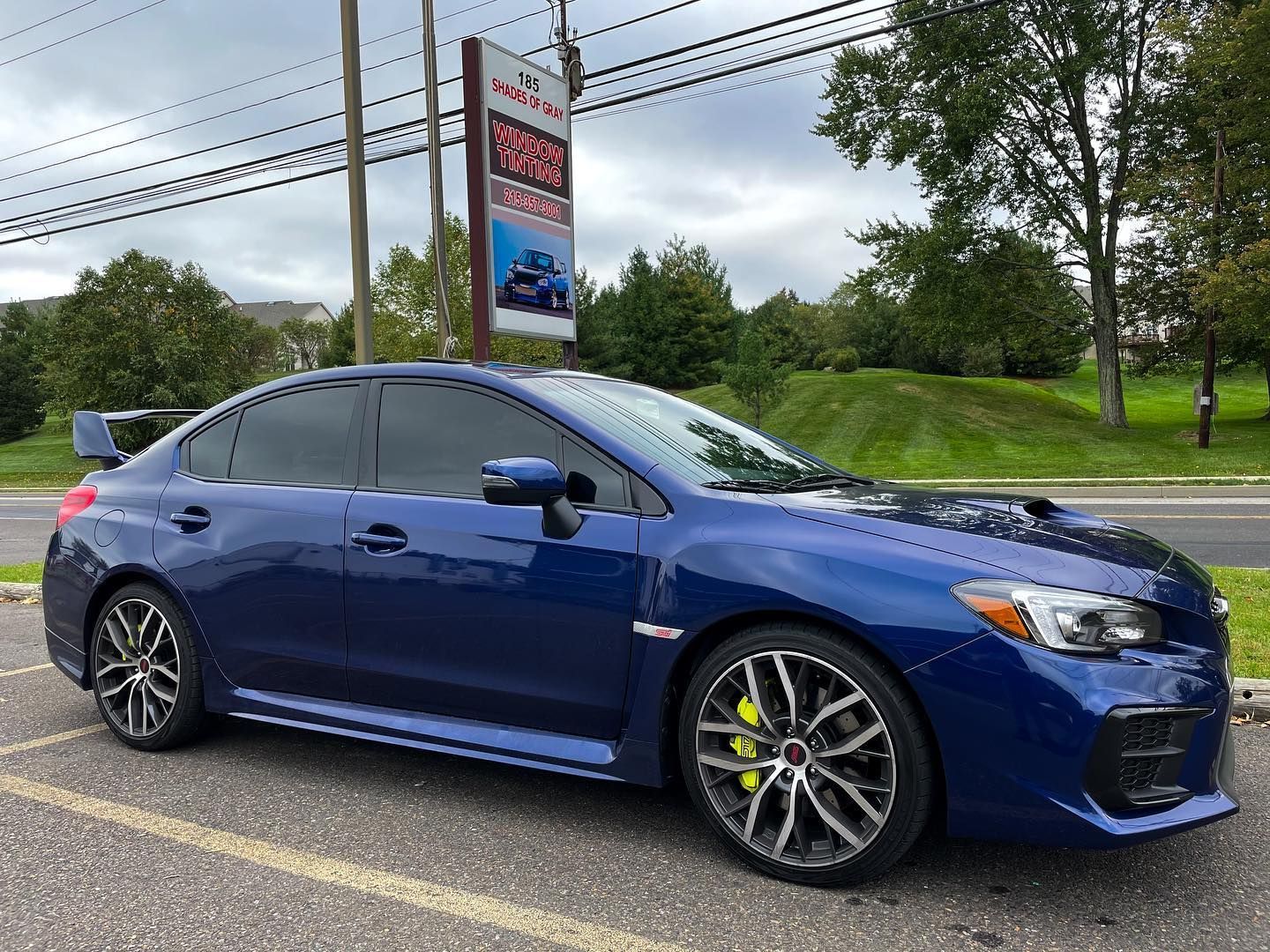 Blue Subaru WRX parked, with tinted windows and spoiler, next to a sign.