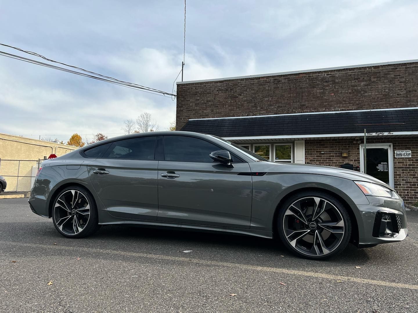 Gray Audi car parked in front of a brick building on a paved surface.
