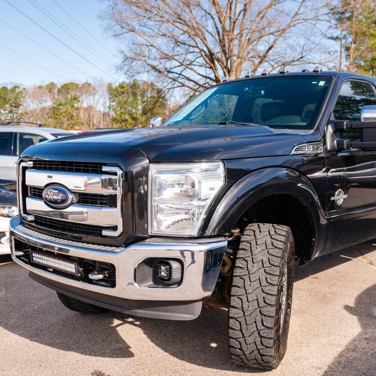 Black Ford pickup truck parked outdoors, chrome accents, large off-road tires, daytime.