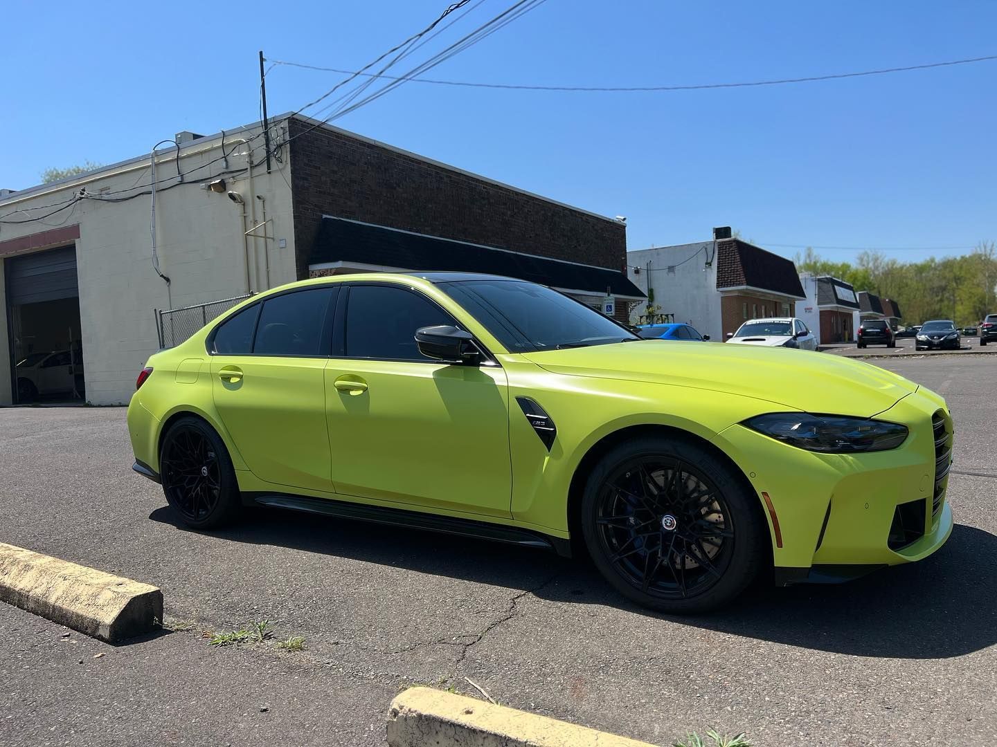 Bright yellow BMW M3 sedan parked on asphalt in front of a building on a sunny day. Black wheels.