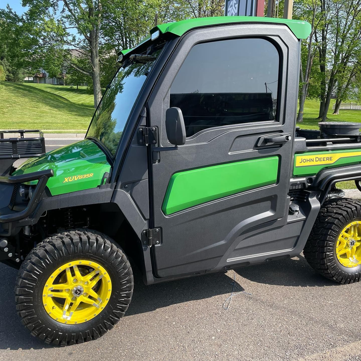 Green and black John Deere Gator utility vehicle with tinted windows and yellow wheels.