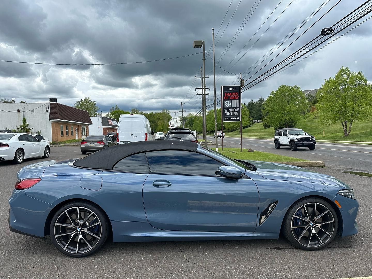 Blue convertible BMW parked on a city street; overcast sky, other vehicles and buildings in the background.
