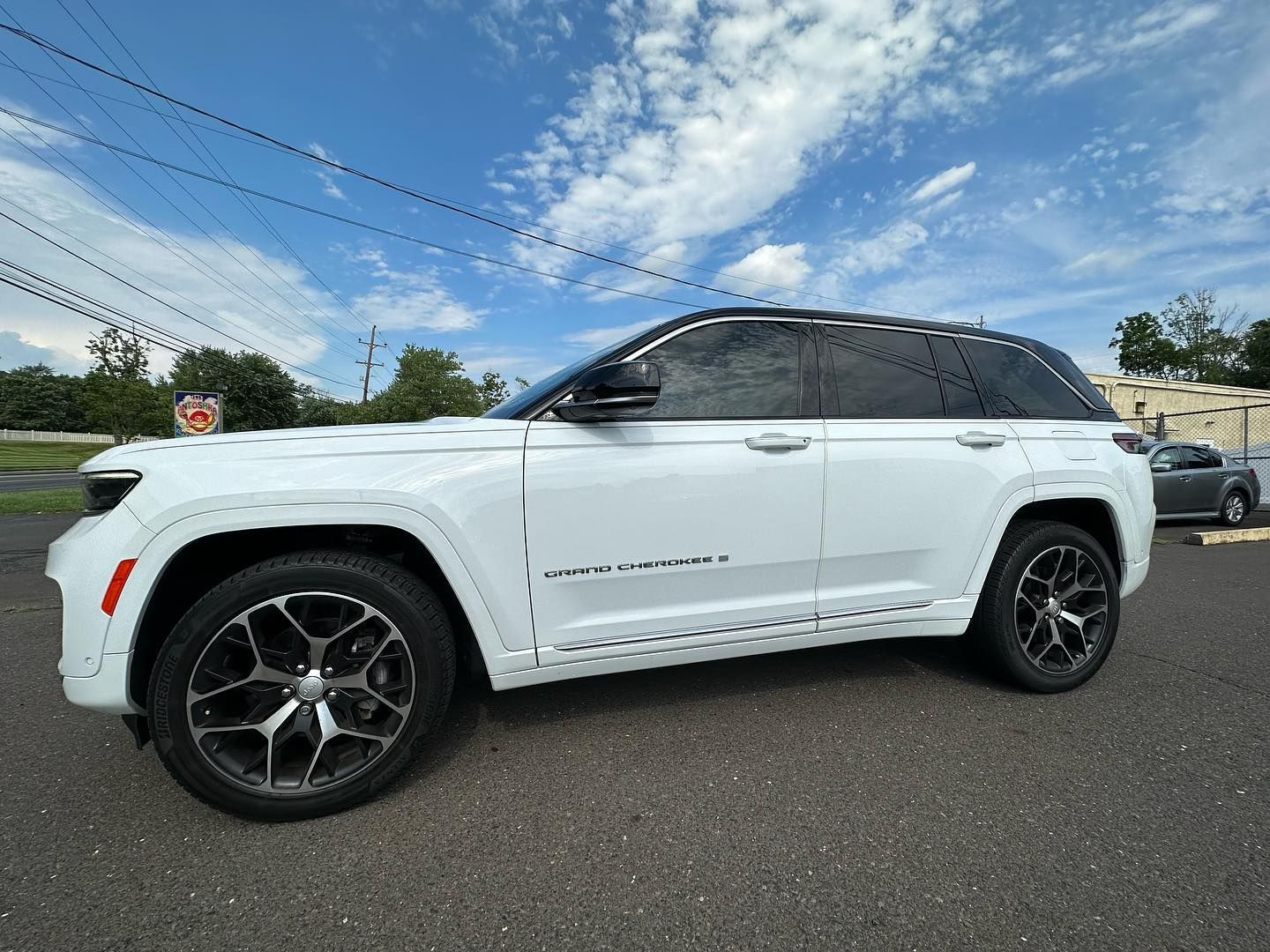 White Jeep Grand Cherokee parked on a road, blue sky overhead.