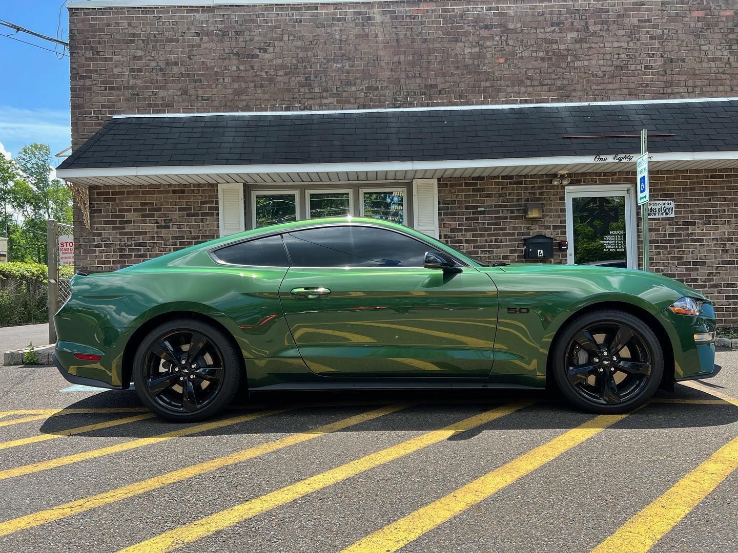 Green Ford Mustang parked in front of a brick building with dark tinted windows.
