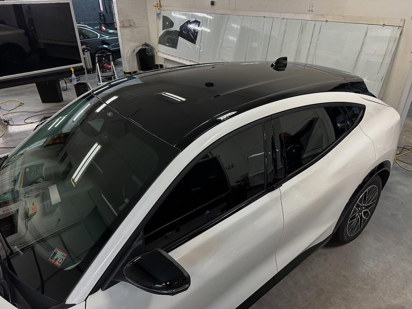 White Ford Mach-E with a black roof and tinted windows in a garage.