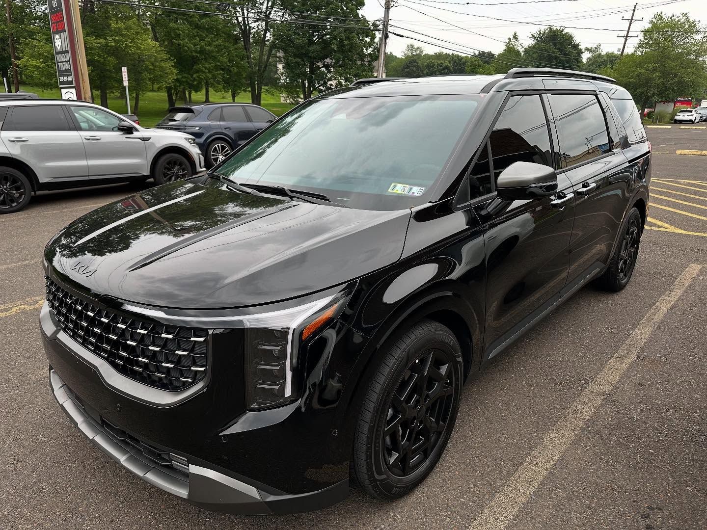 Black Kia Carnival minivan parked outdoors on pavement.