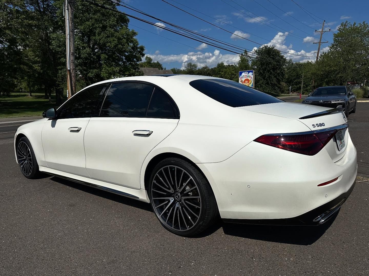 White Mercedes-Benz sedan parked on asphalt, tinted windows, dark rims, sunny outdoor setting.