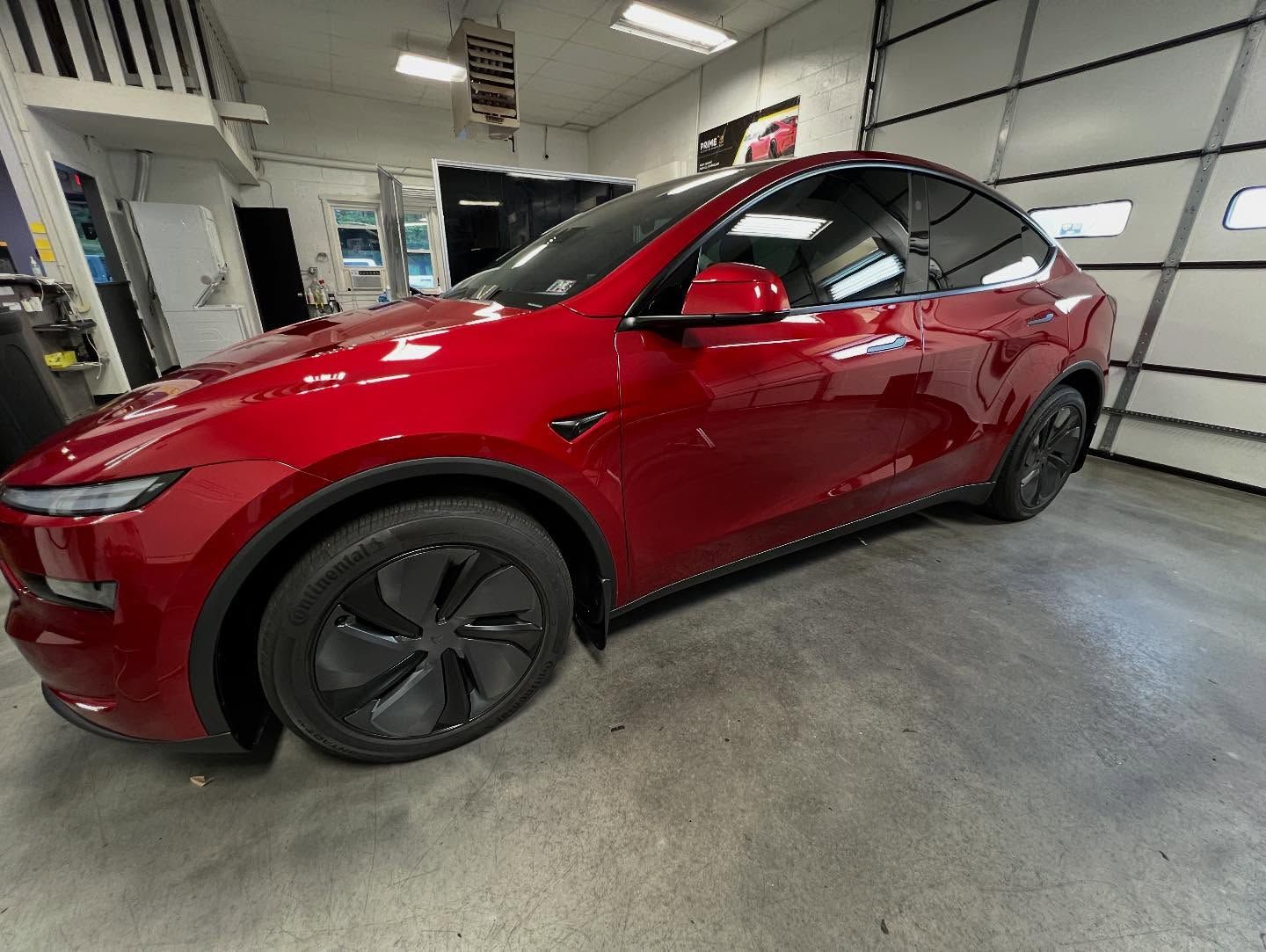 Red Tesla Model Y parked inside a garage, with tinted windows and black wheels.