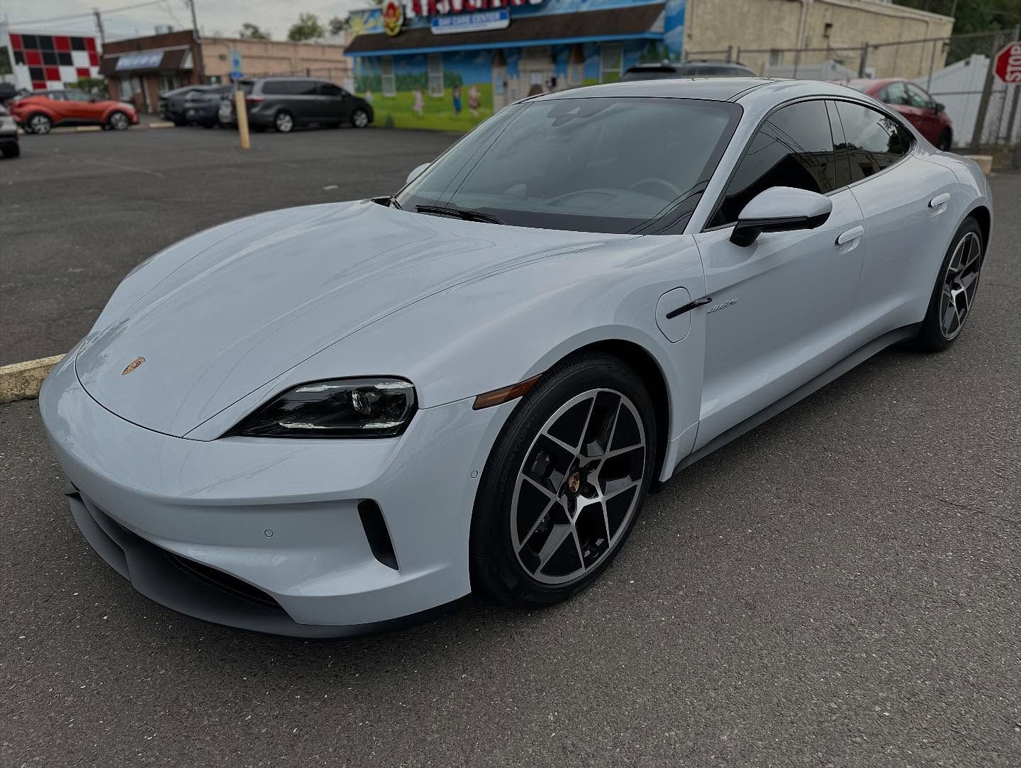 Gray Porsche Taycan electric car parked on asphalt, cloudy day.
