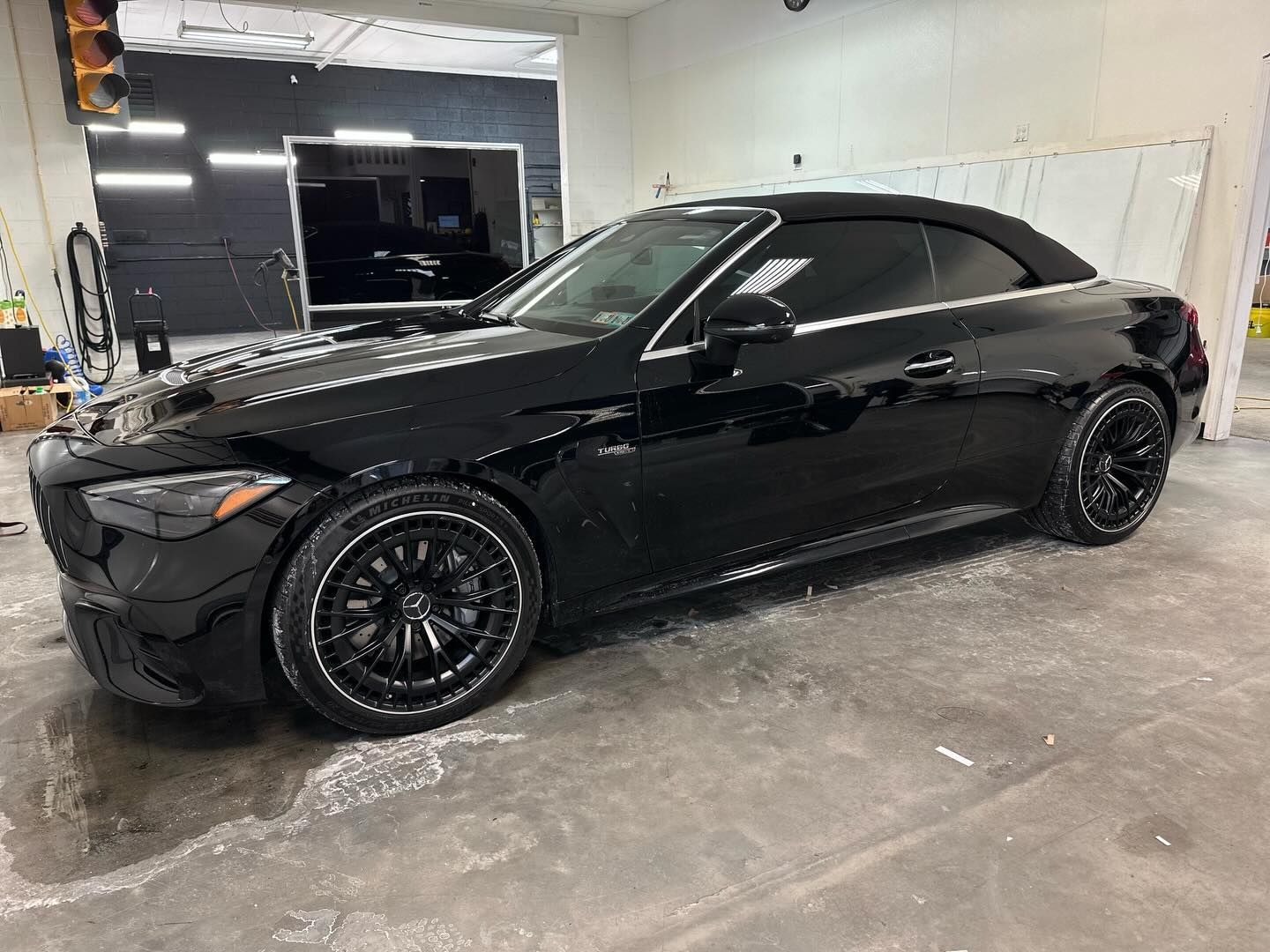 Black convertible car with tinted windows in a workshop setting.