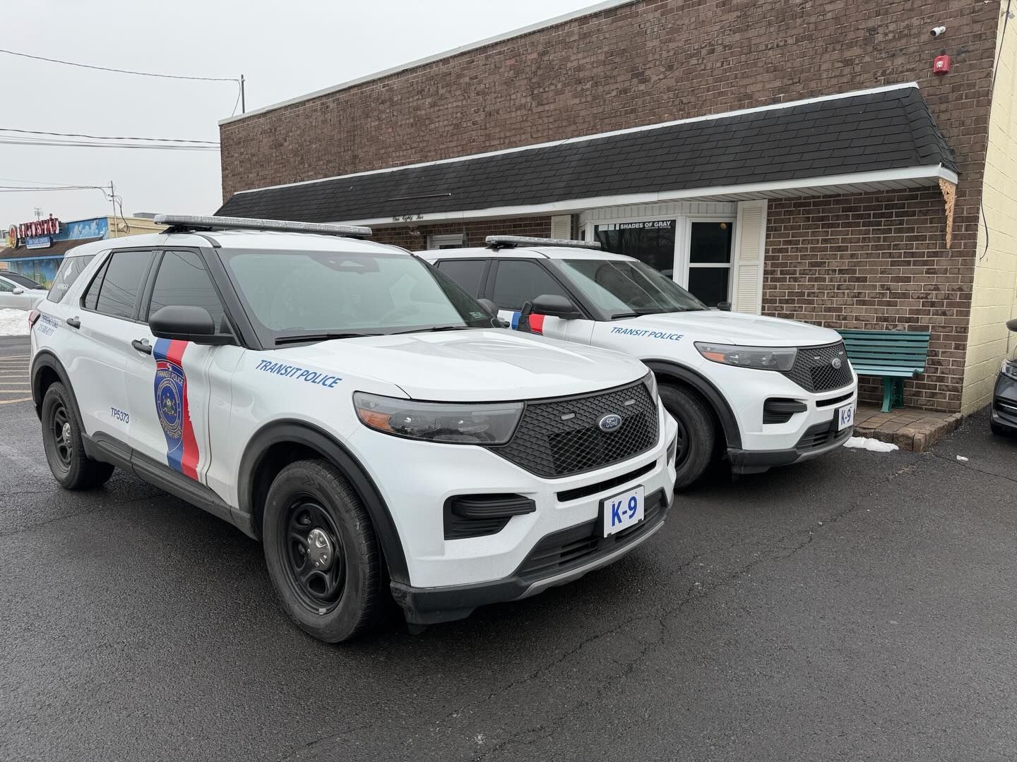 Two white police SUVs parked outside a brown brick building.