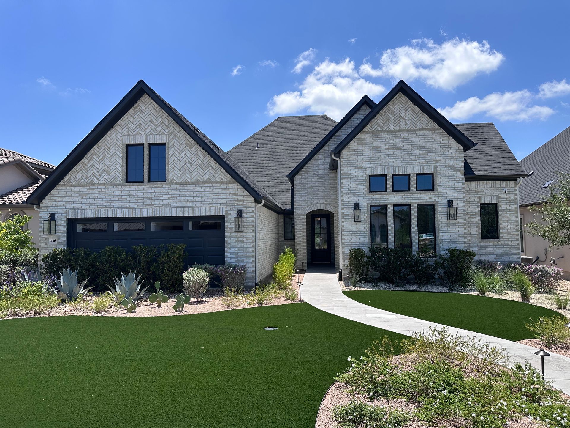 Modern stone suburban house with dark roof, arched windows, and a curved walkway in front.