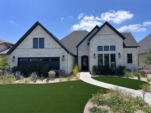 Modern gray brick house with steep gables, black garage doors, and a curved walkway under a blue sky