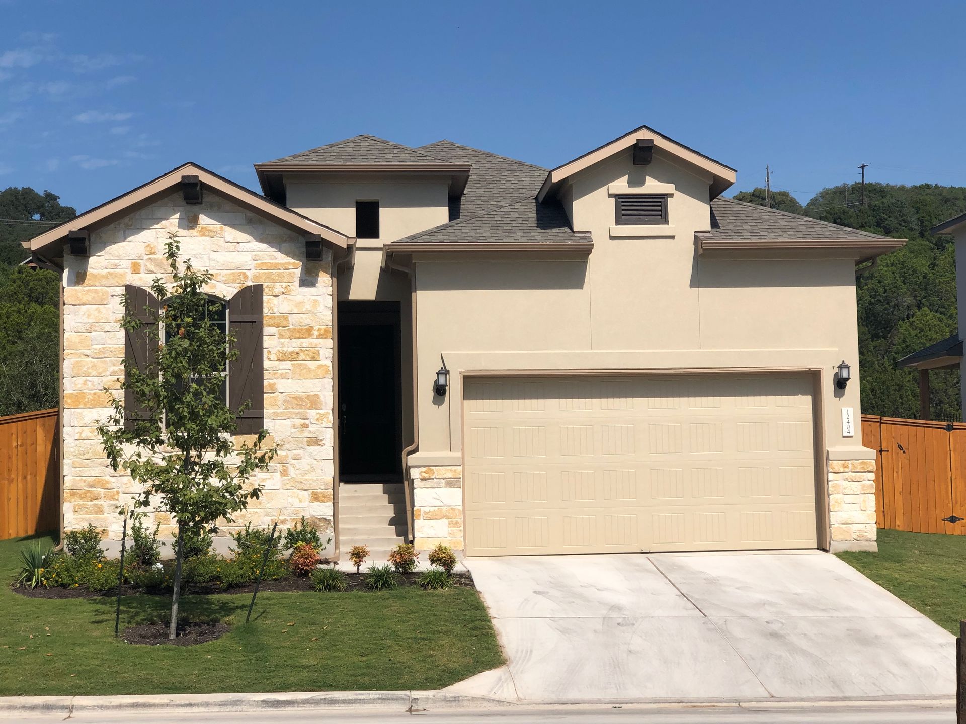 Single-story beige house with stone facade, two-car garage, and a driveway under a clear blue sky