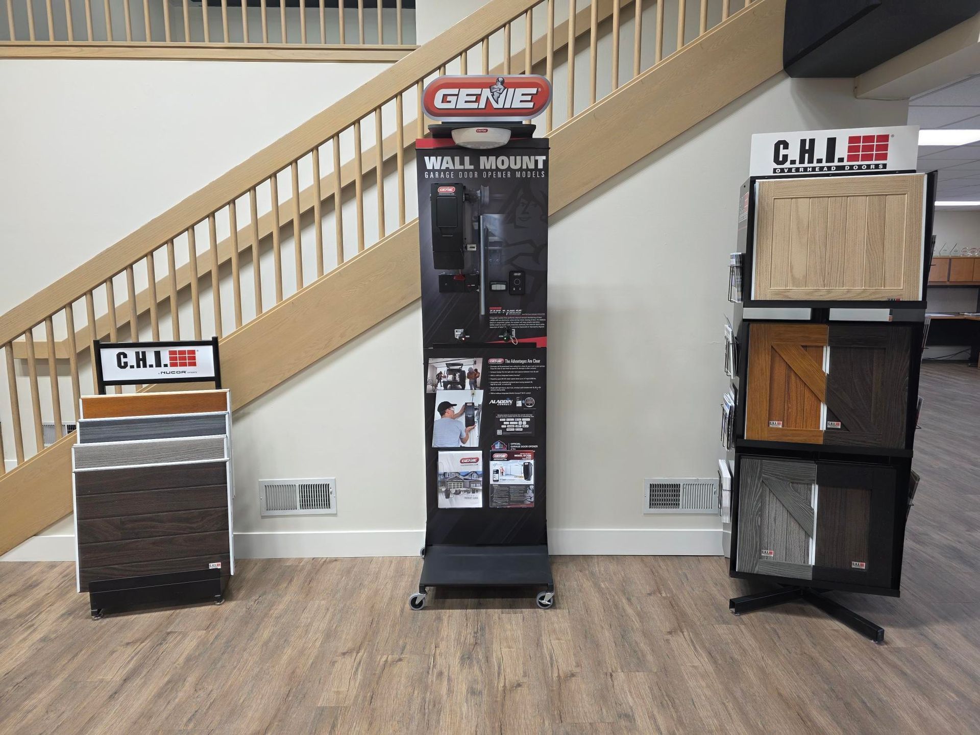 Displays of garage door samples and a Genie wall mount opener in a showroom setting. Staircase in the background.
