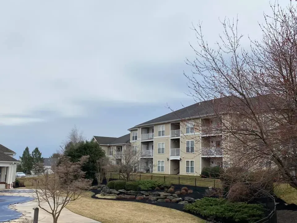 Apartment building under cloudy sky with bare trees and landscaped yard.