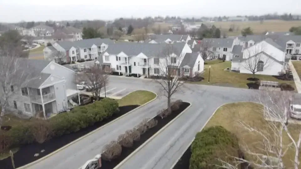 Aerial view of a suburban neighborhood with rows of white townhouses, roads, and green landscaping.