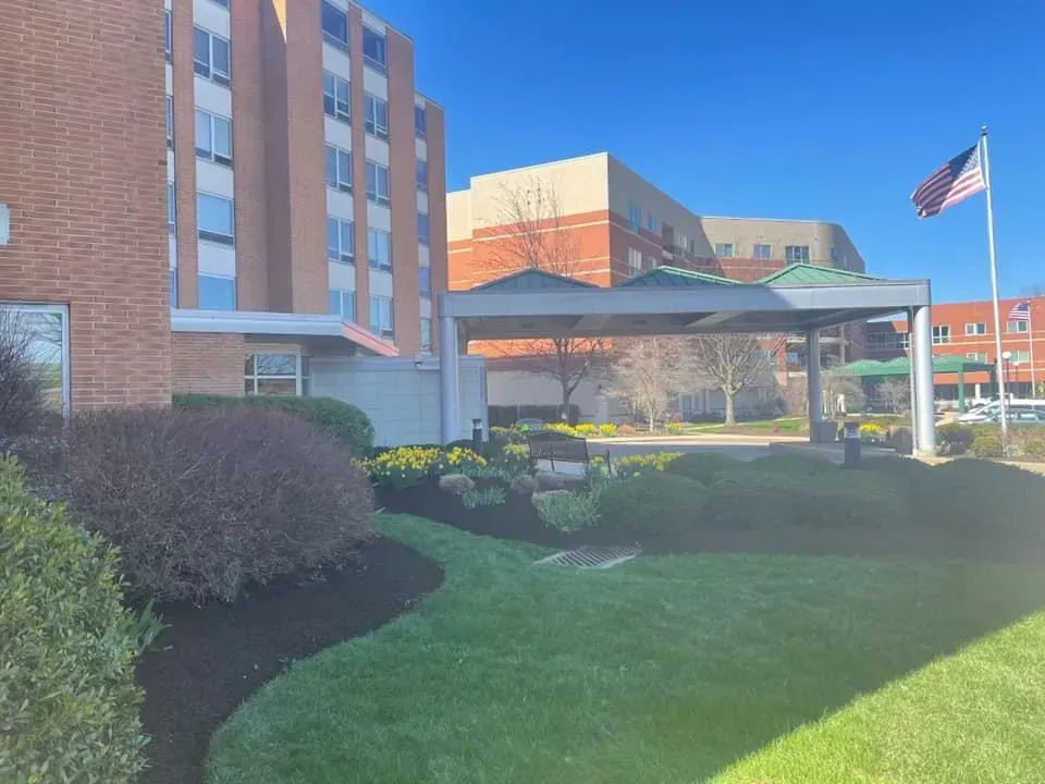 Exterior view of a multi-story brick building with a covered entrance, green grass, and an American flag.