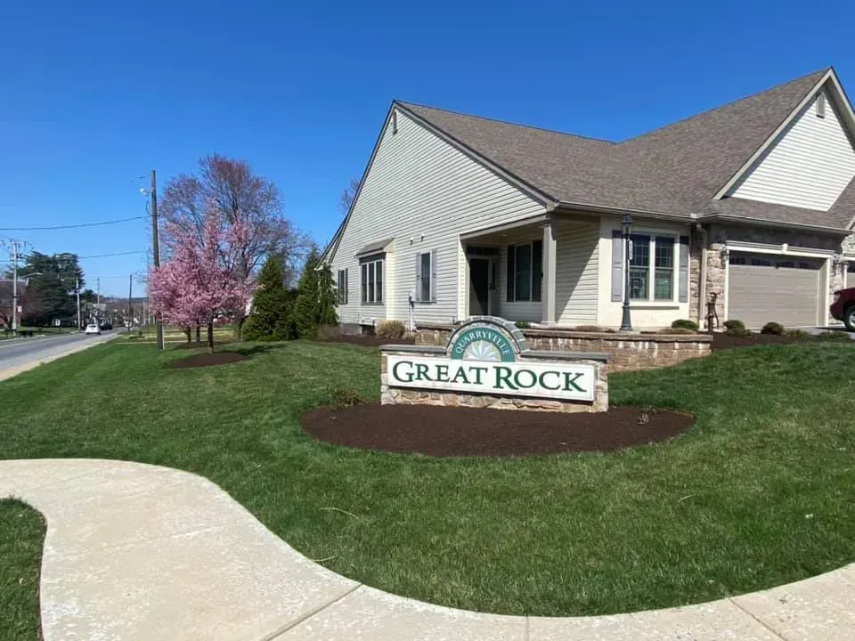 Sign for Great Rock community next to a building, with a curving sidewalk, green lawn, and blue sky.