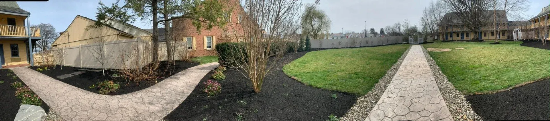 A stone path leading through a green lawn and around buildings with a cloudy sky overhead.