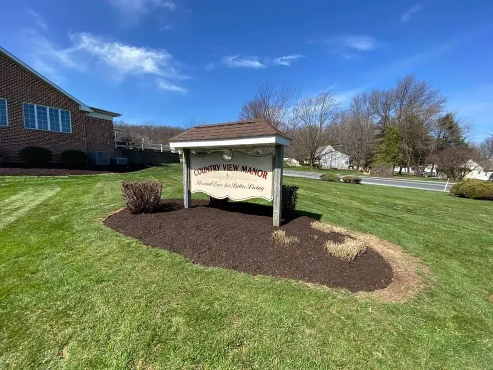 Sign for Copper Hill Ranch, brown roof, beige with brown lettering, set in mulch bed on green lawn.