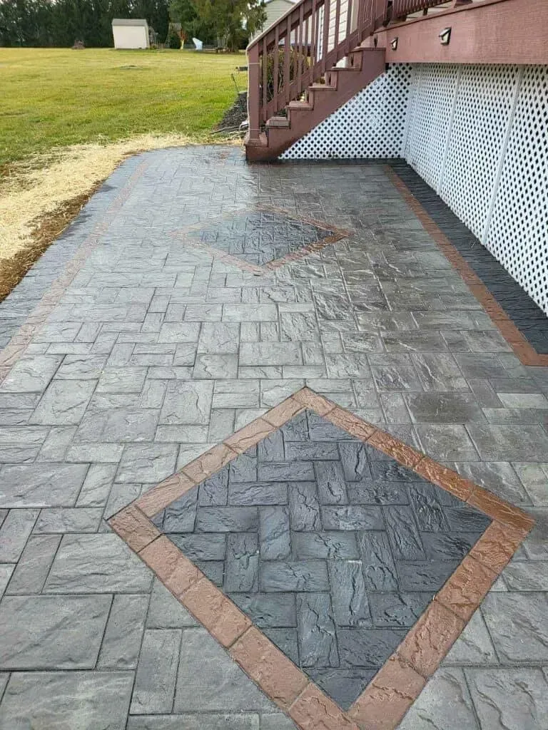 Stamped concrete patio with brick pattern, brown border, and stairs.