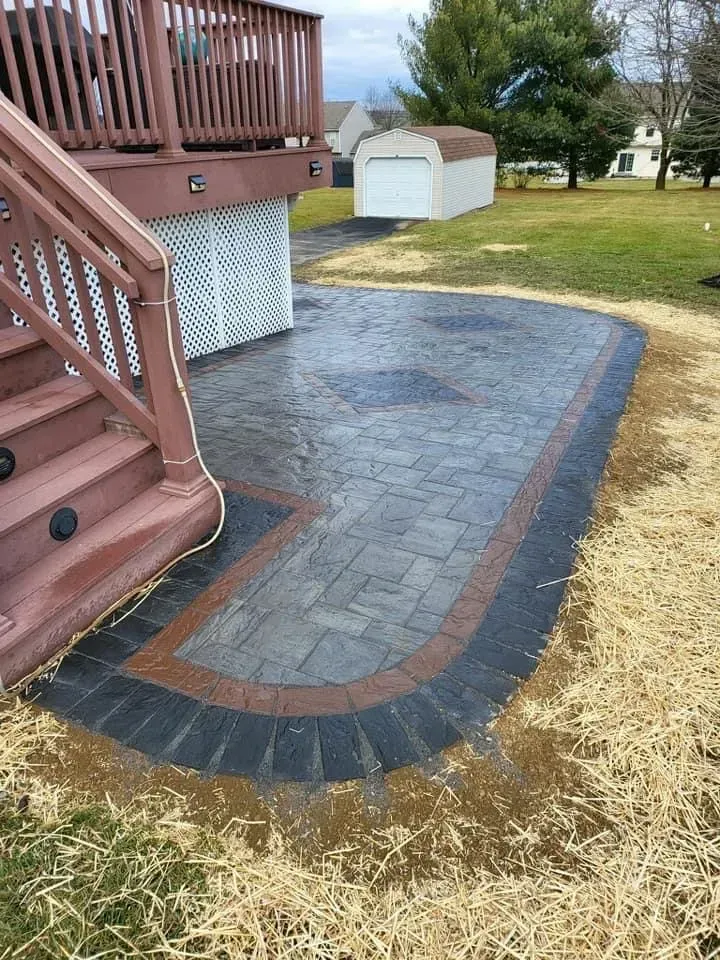 Brick patio under deck, edged with black and brown pavers, on grass.
