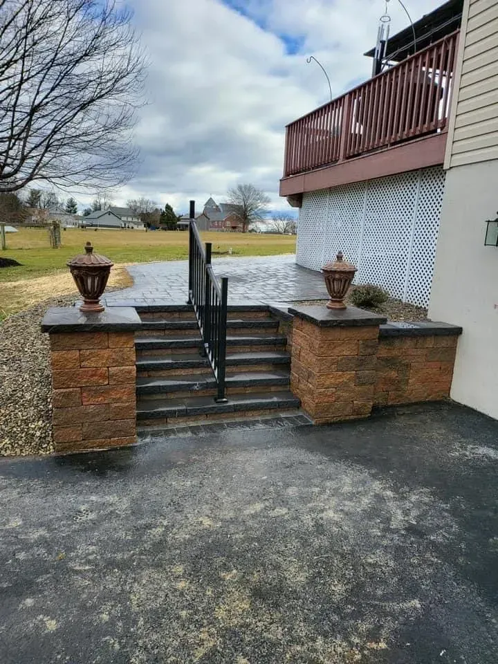 Stone steps with black railing leading to a deck; decorative lanterns atop brick pillars.