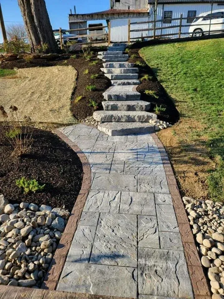 Stone walkway and steps leading up a hill to a building. Landscaping with mulch, rocks, and grass.