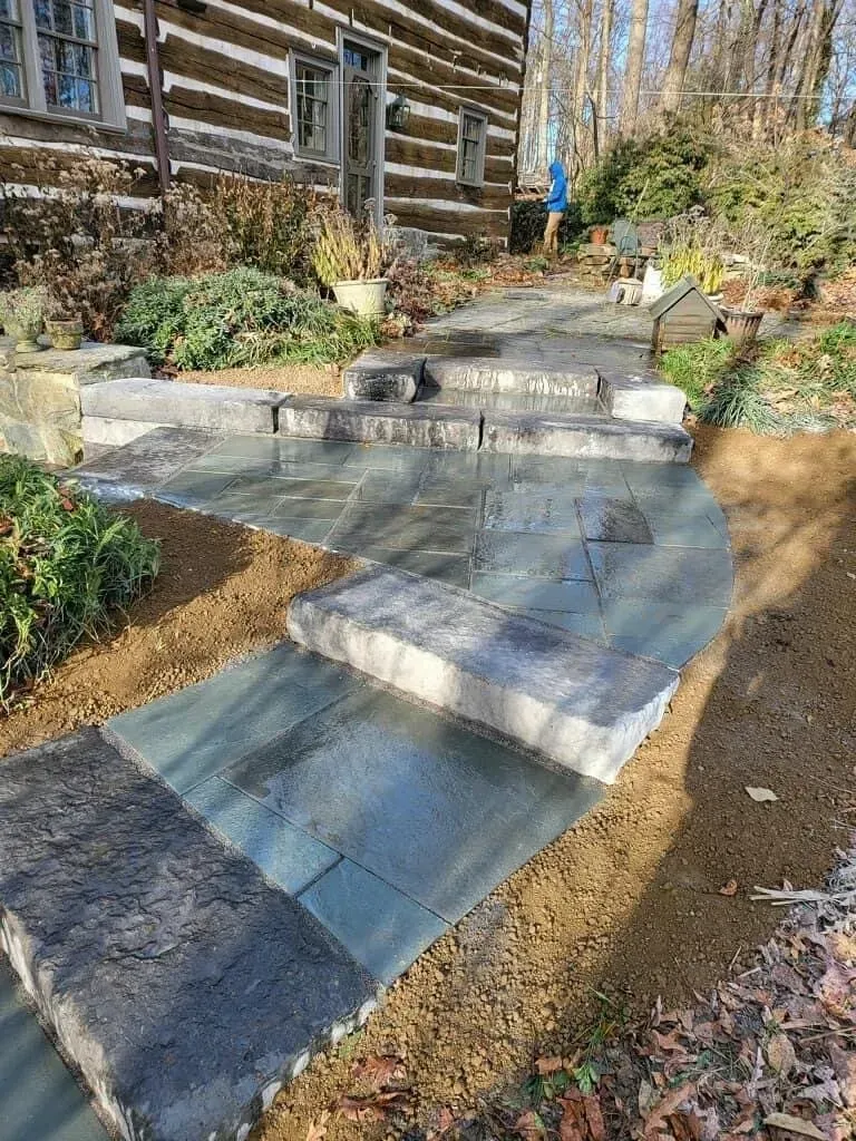 Stone steps and walkway leading to a log cabin, surrounded by dirt and landscaping.