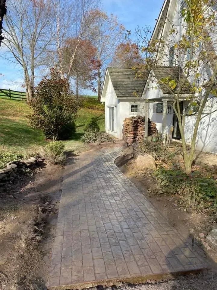 Brick pathway leads to a white building with a small peaked roof; trees and grassy field in the background.